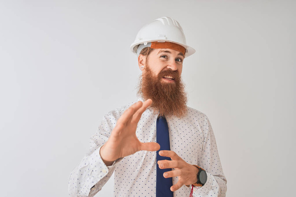 Young redhead irish architect man wearing security helmet over isolated white background disgusted expression, displeased and fearful doing disgust face because aversion reaction. With hands raised. Annoying concept. - Foto, imagen