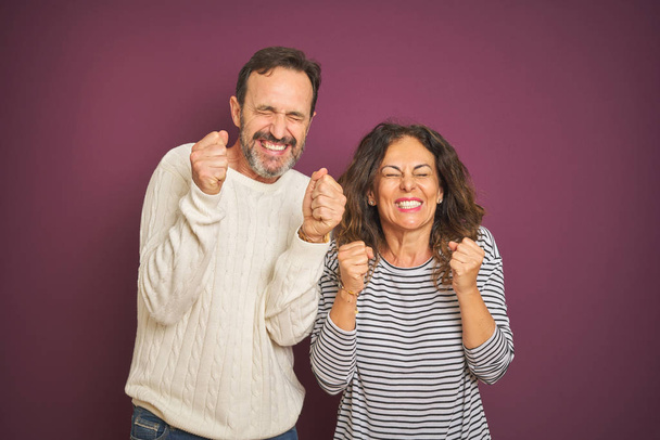 Beautiful middle age couple wearing winter sweater over isolated purple background excited for success with arms raised and eyes closed celebrating victory smiling. Winner concept. - Фото, изображение