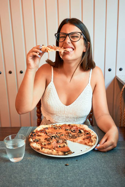 Молода красива жінка, яка сидить в ресторані і насолоджується літньою відпусткою, поїдаючи італійську піцу. - Фото, зображення