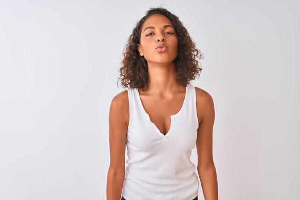 Νεαρή Βραζιλιάνα γυναίκα που φοράει casual t-shirt στέκεται πάνω από απομονωμένο λευκό φόντο κοιτάζοντας την κάμερα φυσώντας ένα φιλί στον αέρα είναι όμορφη και σέξι. Έκφραση αγάπης. - Φωτογραφία, εικόνα