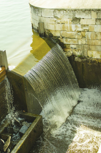 Желто-зеленые сточные воды текут вдоль городских стен. водопады, экологические проблемы и чистая питьевая вода
 - Фото, изображение