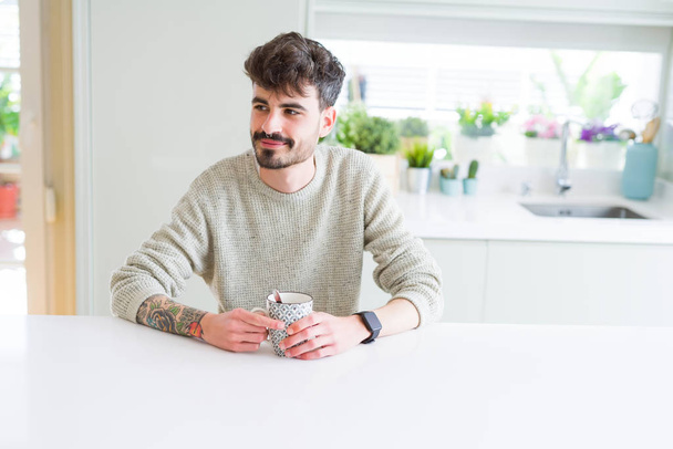 Όμορφος νέος άνθρωπος πίνοντας ένα φλιτζάνι καφέ στο σπίτι, απολαμβάνοντας WA - Φωτογραφία, εικόνα