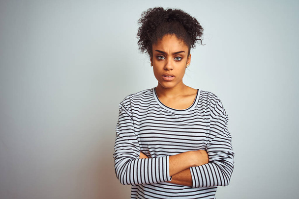Afroameričanka v proužkovaném tričku, stojící nad osamělým bílým pozadím, skeptická a nervózní, nesouhlasící výraz na tváři se zkříženýma rukama. Negativní osoba. - Fotografie, Obrázek