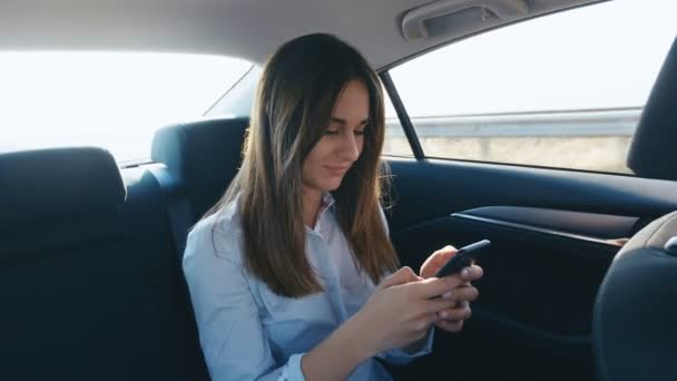 Arckép fiatal nő használ őt smartphone közben utazótáska-ban egy autó-val egy vezető. A lány ellenőrzi mailek, beszélgetések közben lovagol egy taxi - Felvétel, videó