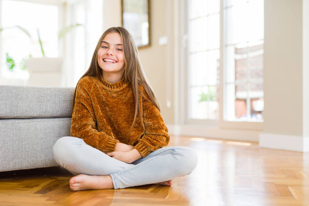 Hermosa niña joven sentada en el suelo en casa con una sonrisa feliz y fresca en la cara. Persona afortunada
. - Foto, imagen