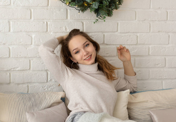 Portrait of smiling young woman sitting in the chair and looking at camera on the white brick wall background - Foto, Imagen