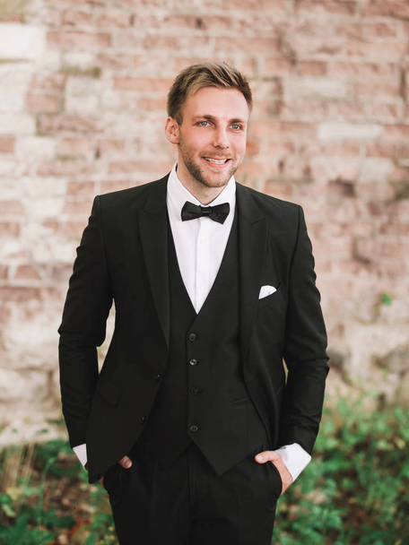 e smiling groom in the background of old brick wall. - Foto, Imagen