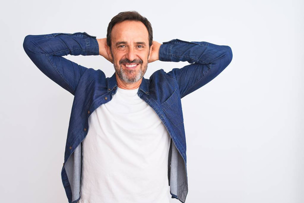 Middle age handsome man wearing blue denim shirt standing over isolated white background relaxing and stretching, arms and hands behind head and neck smiling happy - Photo, Image