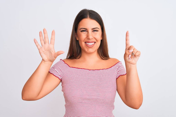 Πορτρέτο της όμορφης νεαρής γυναίκας που στέκεται πάνω από απομονωμένο λευκό φόντο που δείχνει και δείχνει προς τα πάνω με τα δάχτυλα νούμερο έξι, ενώ χαμογελά αυτοπεποίθηση και χαρούμενος. - Φωτογραφία, εικόνα
