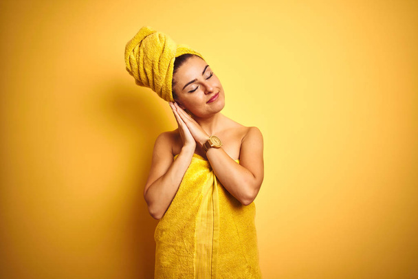 Joven hermosa mujer usando toalla después de la ducha sobre fondo amarillo aislado durmiendo cansado soñando y posando con las manos juntas mientras sonríe con los ojos cerrados
. - Foto, imagen