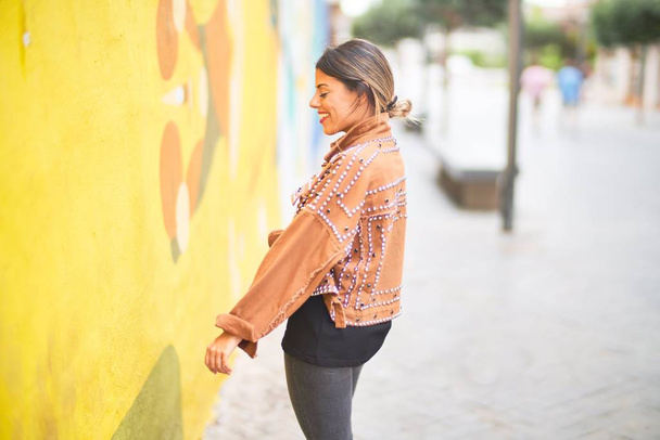jong mooi meisje dragen bruin jasje staan achteruit over kleurrijke muur in de stad straat - Foto, afbeelding
