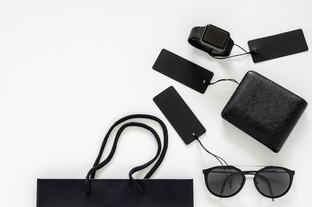 Ploché položení pánských potřeb - černá peněženka, sluneční brýle, chytré hodinky, cenovky a nákupní taška na bílém pozadí pro koncept prodeje Black Friday. - Fotografie, Obrázek