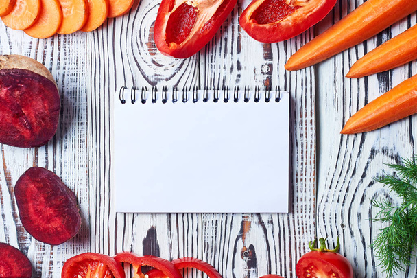 Different natural fresh ripe cutted vegetables near blank paper notepad lies on old white rustic wooden table on kitchen. Healthy food concept. Space for text. Top view - Foto, immagini