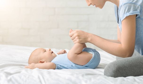 Zorgzame moeder het maken van inspanderende oefeningen met haar pasgeboren zoon - Foto, afbeelding