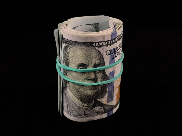 Bankbiljetten van 100 Us dollars op een zwarte achtergrond. Honderd dollar biljetten zijn verdraaid met een elastische band. Amerikaans geld op tafel. - Foto, afbeelding