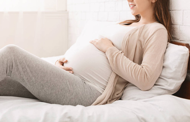 Terhes nő megható hasát, feküdt az ágyon otthon - Fotó, kép