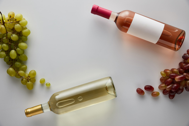 top view of bottles with white and rose wine near grape on white background - Photo, Image