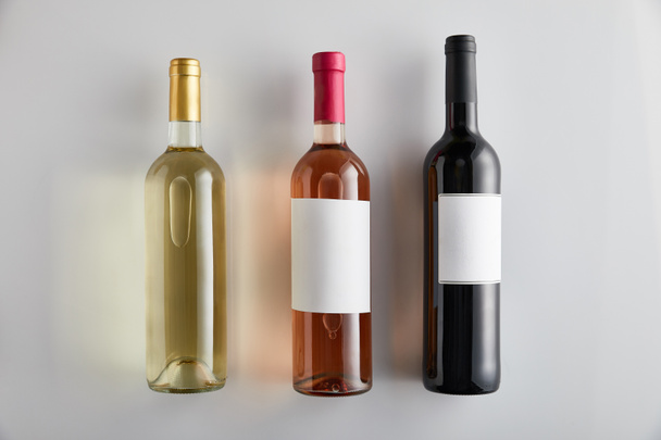 επίπεδο θέσει με μπουκάλια με λευκό, τριαντάφυλλο και κόκκινο κρασί σε λευκό φόντο - Φωτογραφία, εικόνα