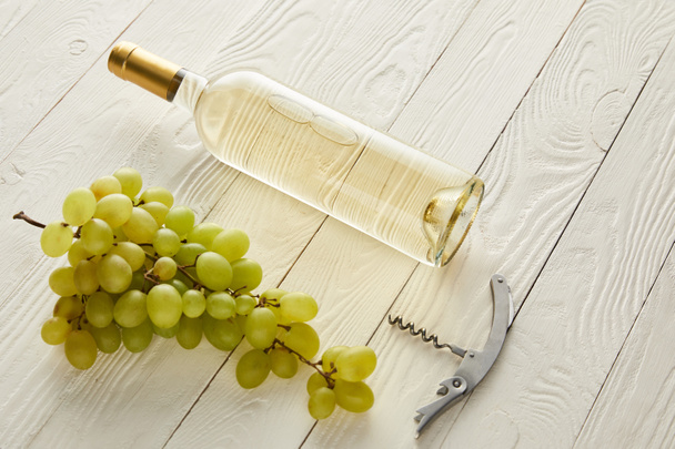 bottle with white wine near grape and corkscrew on white wooden surface - Valokuva, kuva