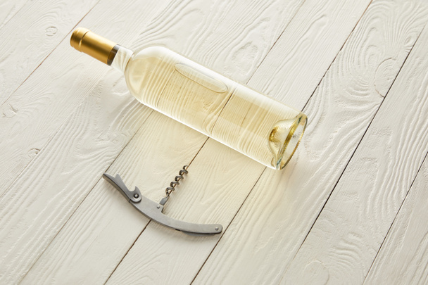 Flasche mit Weißwein nahe Korkenzieher auf weißer Holzoberfläche - Foto, Bild