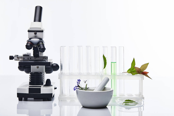 стеклянные пробирки, раствор с пестиком рядом с растениями и микроскоп, изолированные на белом
 - Фото, изображение