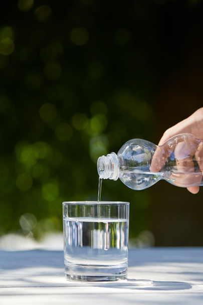 cropped view of man pouring clean water from plastic bottle into glass - Photo, Image