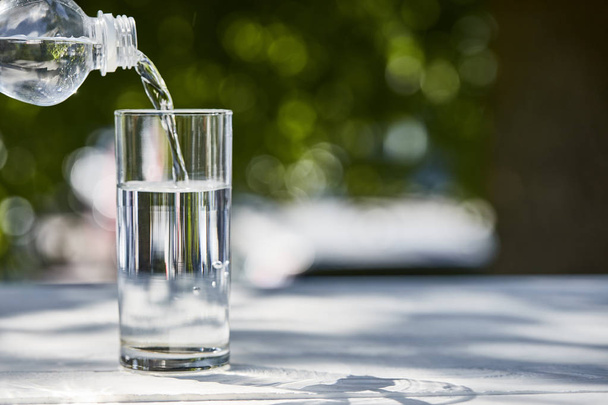 Frisches sauberes Wasser aus der Flasche in transparentem Glas an sonnigen Tagen auf dem Holztisch - Foto, Bild