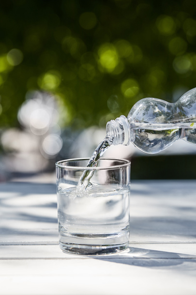 eau propre fraîche coulant de la bouteille en verre transparent à la journée ensoleillée sur une table en bois
 - Photo, image
