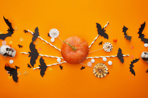 top view of pumpkin, skulls, bats and spiders with confetti on orange background, Halloween decoration - 写真・画像