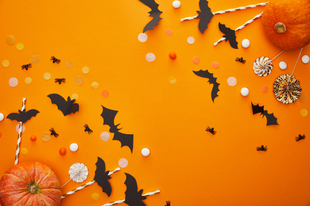 Draufsicht auf Kürbis, Fledermäuse und Spinnen mit Konfetti auf orangefarbenem Hintergrund, Halloween-Dekoration - Foto, Bild