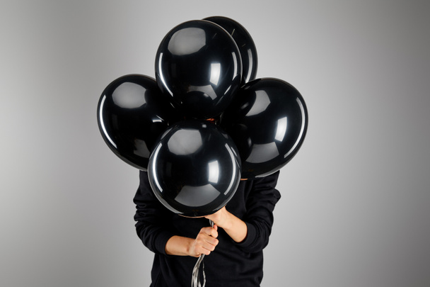 woman holding bunch of black balloons in front of face isolated on grey, black Friday concept - Foto, imagen