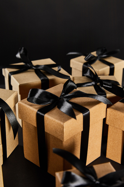 selective focus of cardboard gift boxes with black ribbons isolated on black, black Friday concept - Fotografie, Obrázek