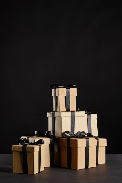 stack of cardboard gift boxes with black ribbons isolated on black, black Friday concept - Photo, Image