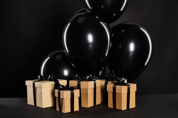 bunch of black balloons near gift boxes isolated on black, black Friday concept - Zdjęcie, obraz