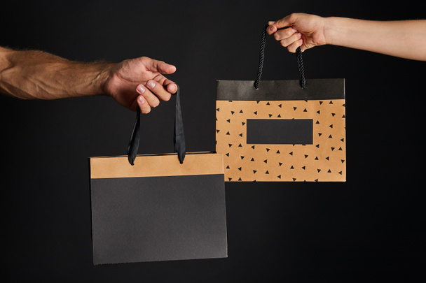 částečný pohled na ženu a muže držící papírové nákupní tašky izolované na černé, černý páteční koncept - Fotografie, Obrázek