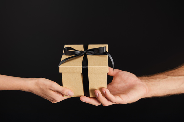 cropped view of man and woman holding cardboard gift box with ribbon isolated on black, black Friday concept - Fotó, kép