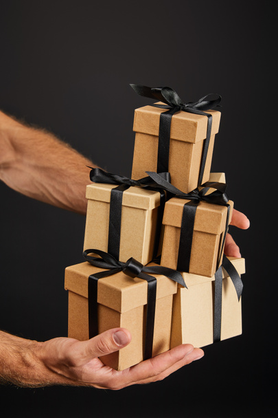 обрізаний вид людини, що тримає картонні подарункові коробки зі стрічками ізольовані на чорній, чорній концепції п'ятниці
 - Фото, зображення