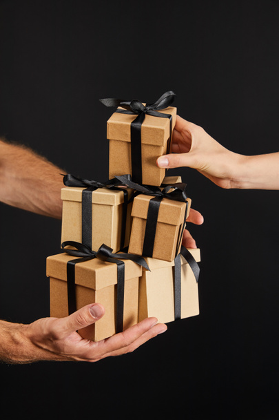 cropped view of man and woman holding cardboard gift boxes with ribbons isolated on black, black Friday concept - Photo, Image