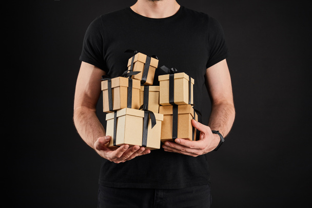 cropped view of man holding cardboard gift boxes with ribbons isolated on black, black Friday concept - Photo, image