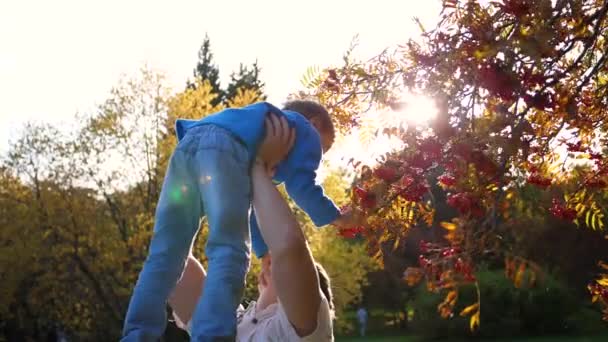 Een jonge vader speelt met een kind, houdt hem in zijn armen, gooit omhoog. De zonnen stralen door het kind. Het lachen en de vreugde van het gezin. - Video