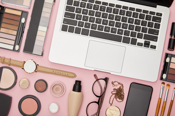 top view of laptop near decorative cosmetics and glasses isolated on pink  - Photo, Image