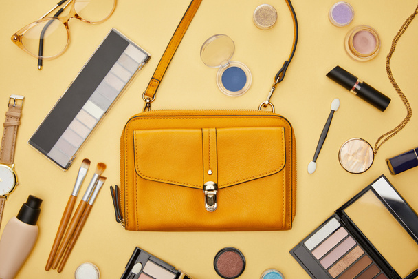 vista superior de la bolsa cerca de cosméticos decorativos y collar aislado en amarillo
  - Foto, Imagen
