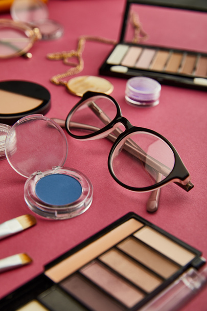selective focus of glasses near decorative cosmetics on crimson  - Photo, Image
