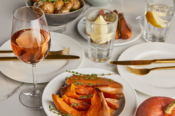 Ψητή κολοκύθα και ποτήρια με λεμονόνερο και ροζέ κρασί σε μαρμάρινο τραπέζι - Φωτογραφία, εικόνα