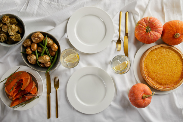 top view of served dinner with pumpkin pie, baked vegetables and fresh whole pumpkins on white tablecloth - Foto, afbeelding
