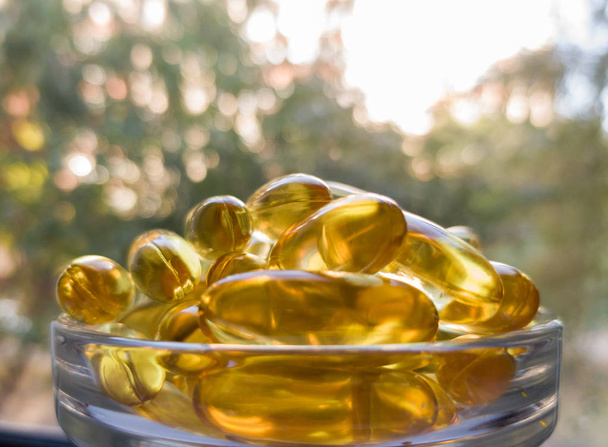 Fish oil capsules in a transparent plate. A lot of vitamin omega-3 against the background of nature and the park. Close up, high resolution product. Metabolism in the body. The body of calcium. A quic - Photo, Image