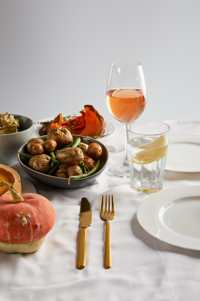 baked potatoes, sliced and whole pumpkin near glasses with rose wine and lemon water isolated on grey - Photo, Image