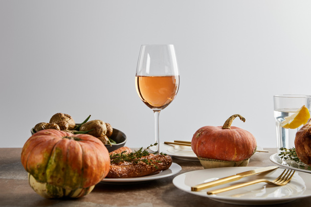 whole pumpkins near baked potatoes and carrots, and glasses with rose wine and lemon water isolated on grey - 写真・画像