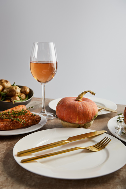 piatto con coltello dorato e forchetta vicino zucca intera e bicchiere con vino rosato isolato su grigio
 - Foto, immagini