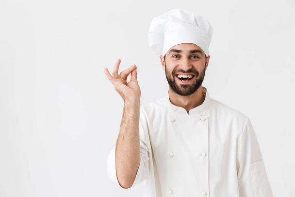 Cheerful pleased young chef posing isolated over white wall background in uniform. - 写真・画像